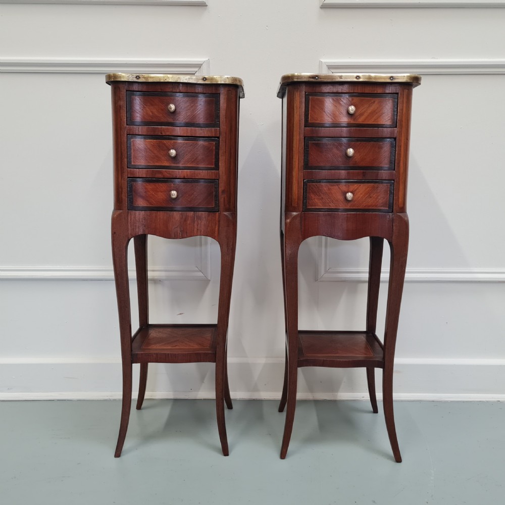 A pair of tall French kingwood bedside cabinets featuring three drawers, brass galleries, slender legs, and lower shelves.