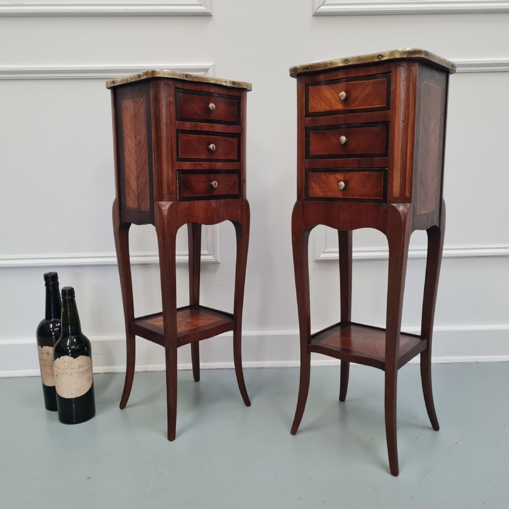 A pair of tall French kingwood bedside cabinets featuring three drawers, brass galleries, slender legs, and lower shelves. View V