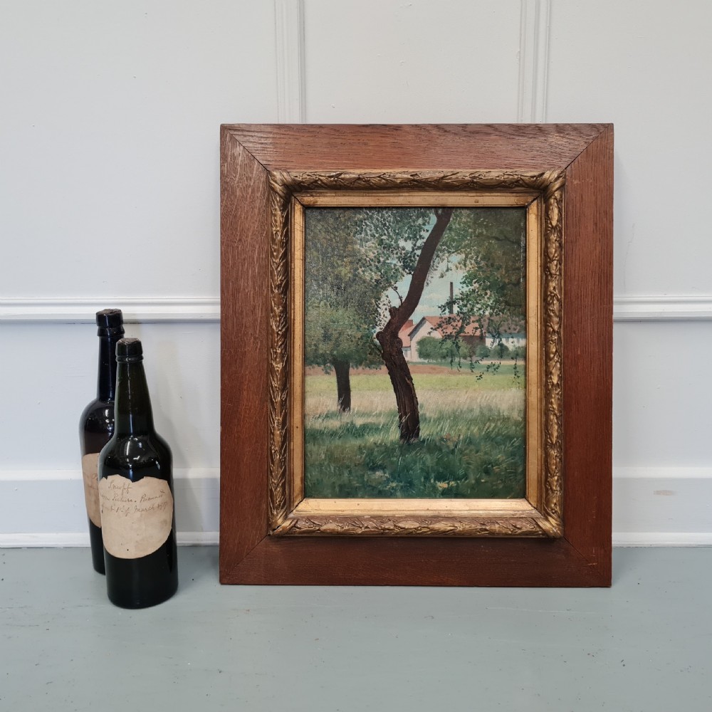 An antique French oil painting depicting trees in a grassy field with a tiled building in the background, set in a carved gilt inner frame and wide oak outer frame. View III
