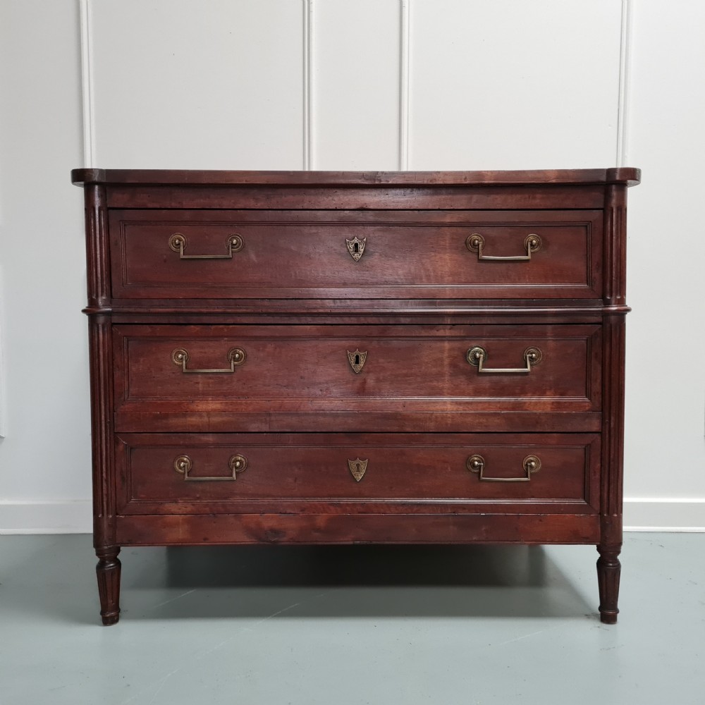 An early antique French cherry commode featuring three long drawers with brass drop handles and escutcheons.
