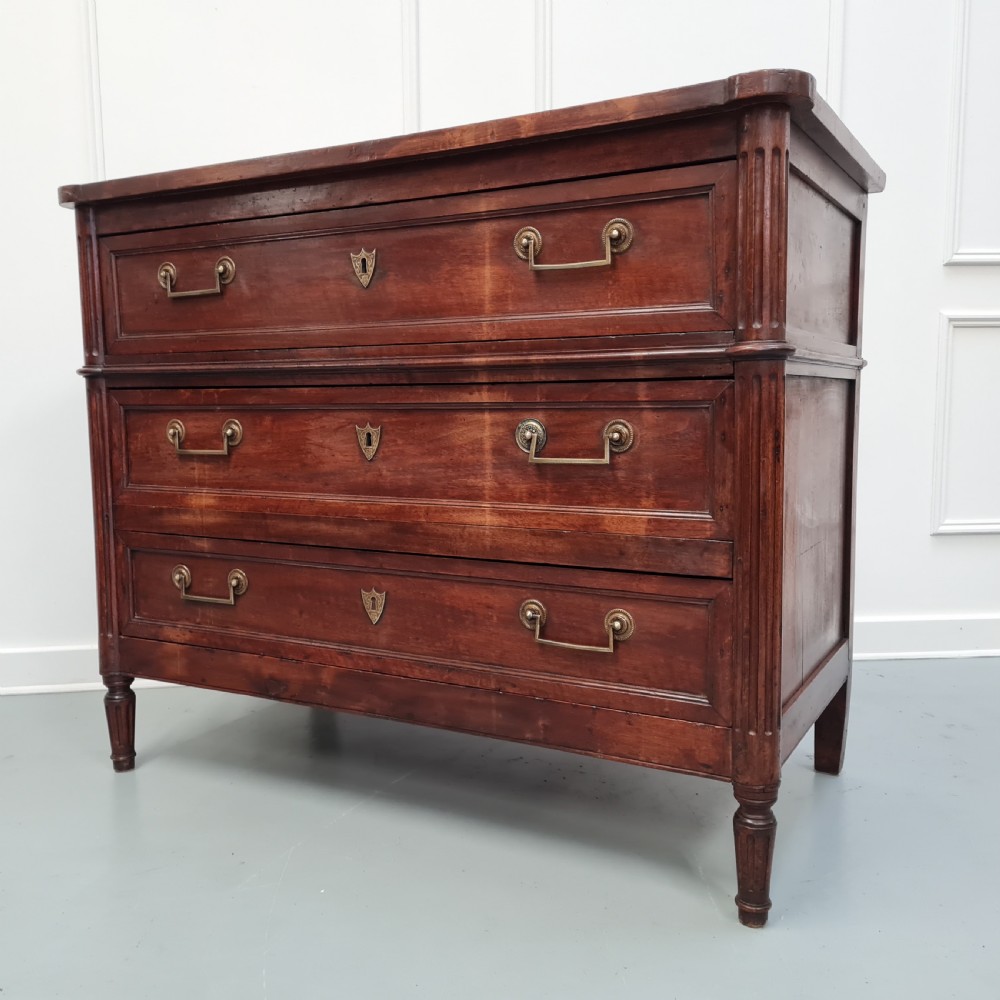 An early antique French cherry commode featuring three long drawers with brass drop handles and escutcheons. View II