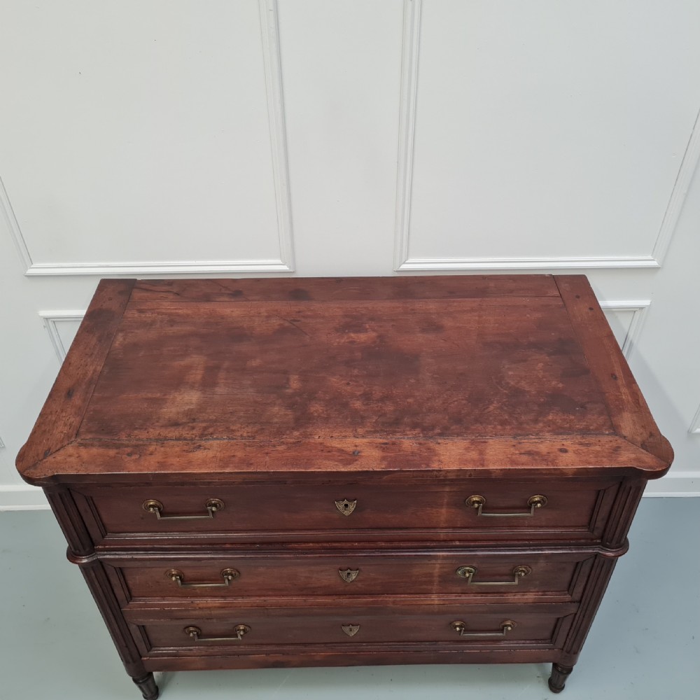 An early antique French cherry commode featuring three long drawers with brass drop handles and escutcheons. View IV