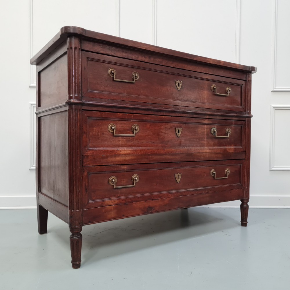 An early antique French cherry commode featuring three long drawers with brass drop handles and escutcheons. View IX