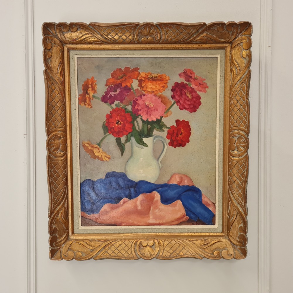 A mid-century still life oil painting depicting a colourful arrangement of flowers in a white pitcher over draped fabric, set within a carved gold frame.
