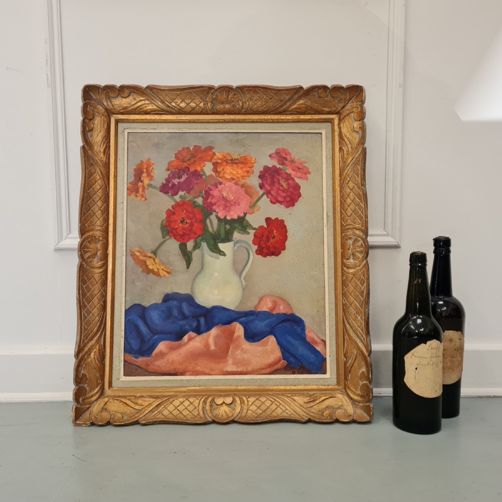 A mid-century still life oil painting depicting a colourful arrangement of flowers in a white pitcher over draped fabric, set within a carved gold frame. View IV