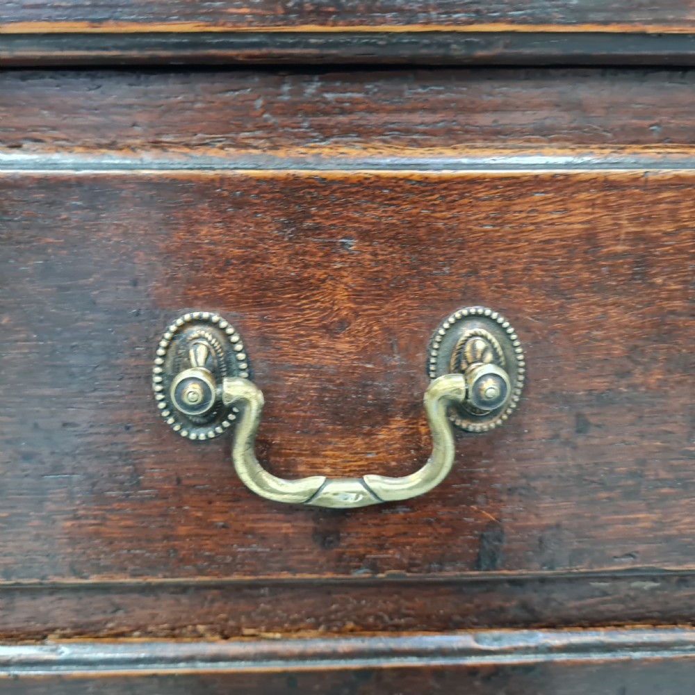 A dark oak Georgian chest of drawers featuring two short drawers over three long drawers with brass swan-neck handles and bracket feet. View II