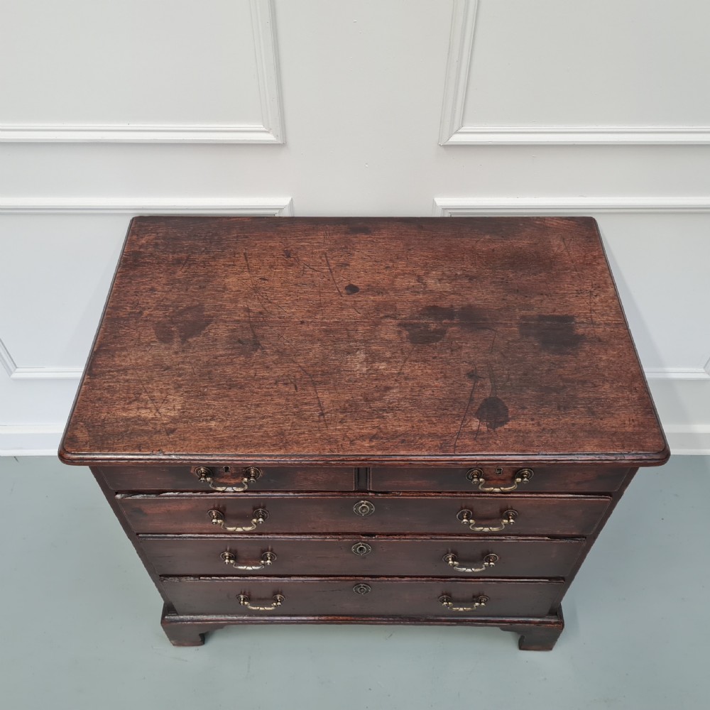 A dark oak Georgian chest of drawers featuring two short drawers over three long drawers with brass swan-neck handles and bracket feet. View IV