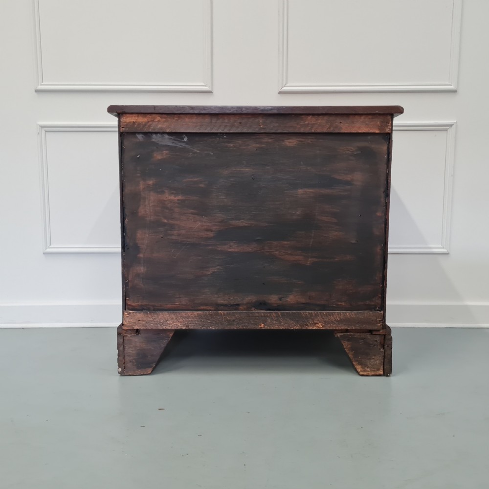 A dark oak Georgian chest of drawers featuring two short drawers over three long drawers with brass swan-neck handles and bracket feet. View VI