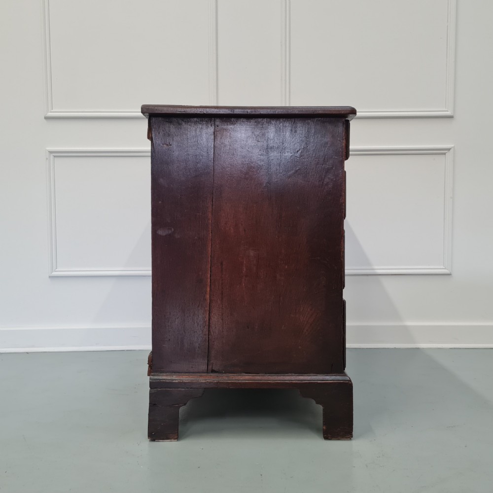 A dark oak Georgian chest of drawers featuring two short drawers over three long drawers with brass swan-neck handles and bracket feet. View VII
