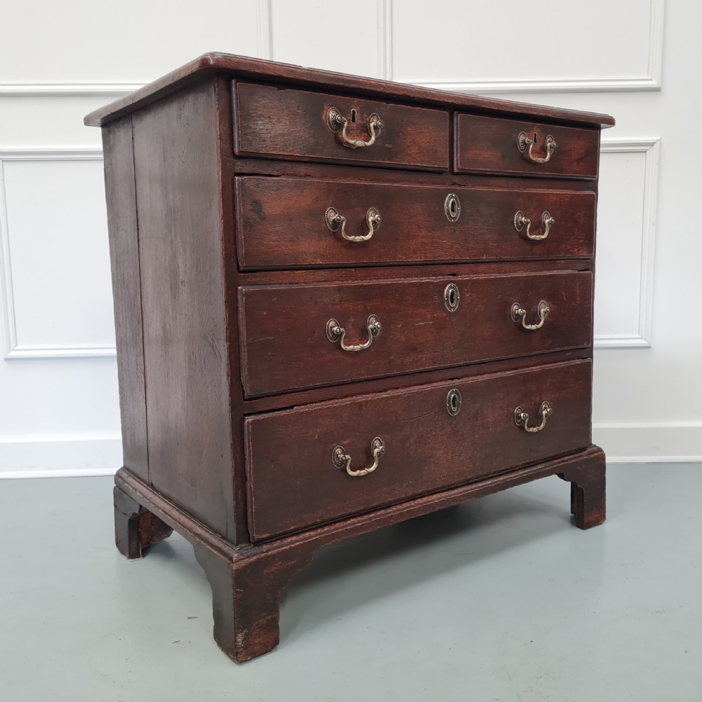 A dark oak Georgian chest of drawers featuring two short drawers over three long drawers with brass swan-neck handles and bracket feet. View VIII