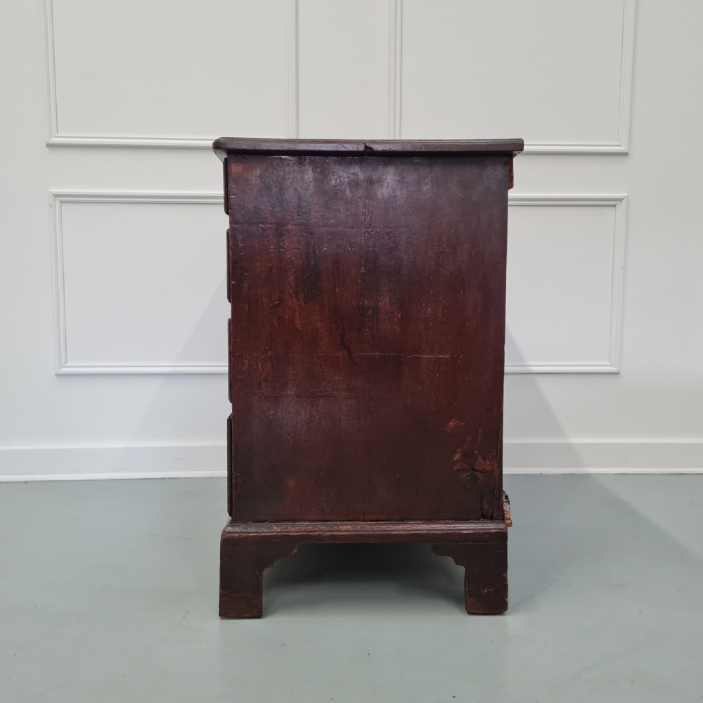 A dark oak Georgian chest of drawers featuring two short drawers over three long drawers with brass swan-neck handles and bracket feet. View IX
