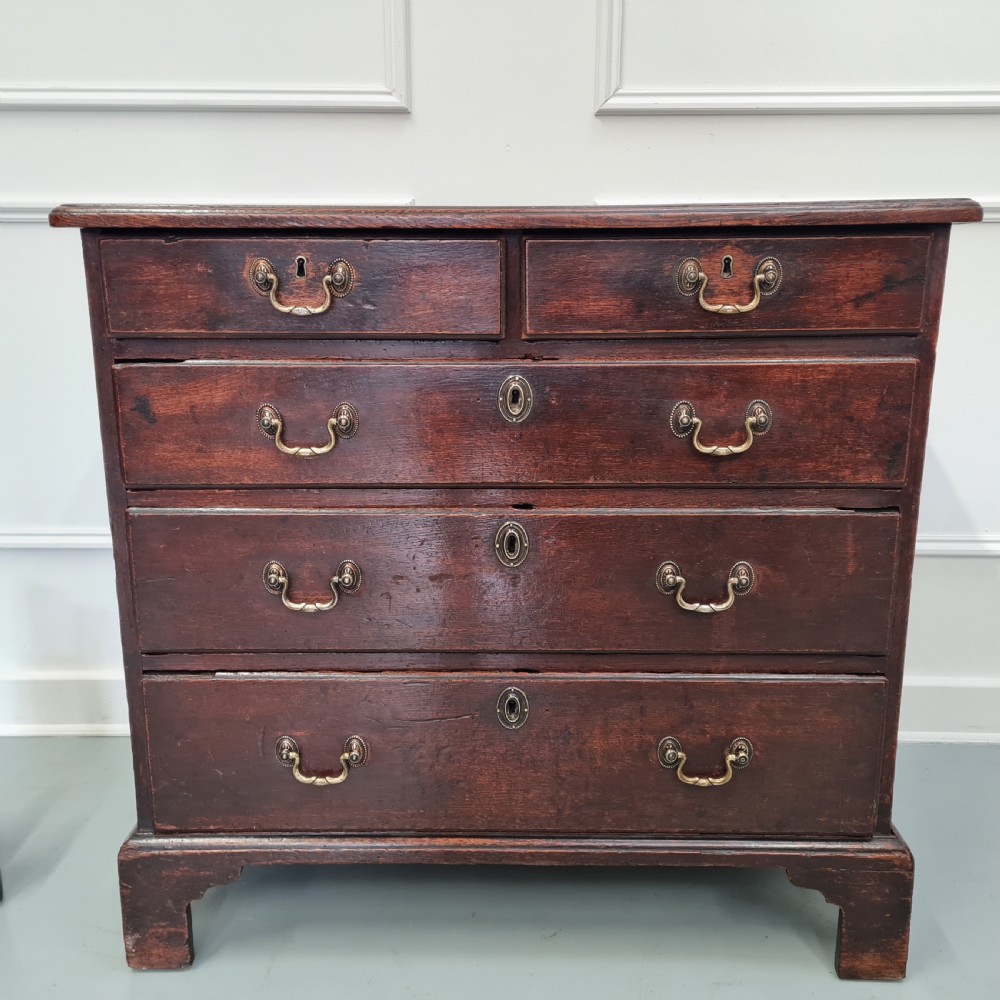 A dark oak Georgian chest of drawers featuring two short drawers over three long drawers with brass swan-neck handles and bracket feet. View XI