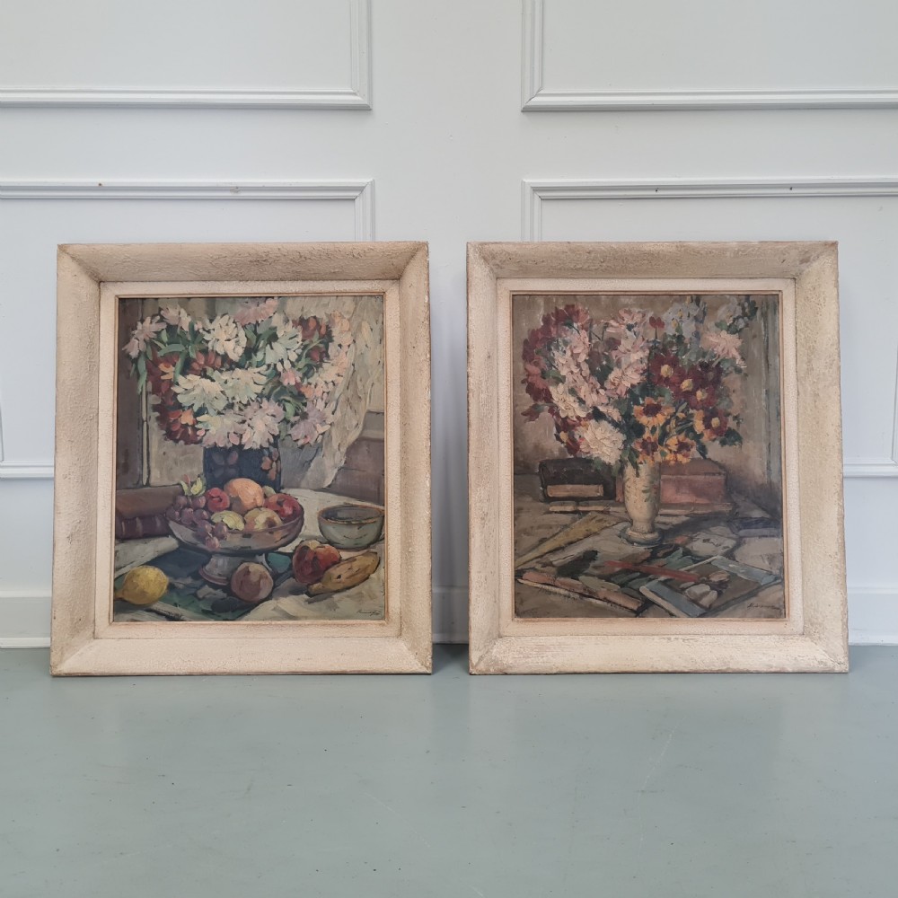 A pair of framed 1930s oil paintings depicting floral arrangements and fruit still life compositions in cream painted wooden frames.