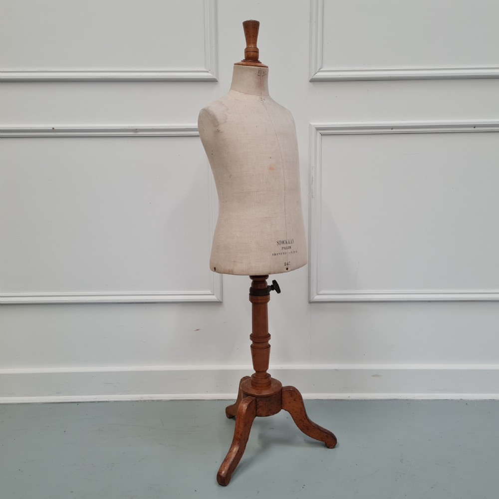 An antique French child-sized tailor mannequin by Stockman featuring a beige linen torso mounted on a turned wooden tripod stand. View V