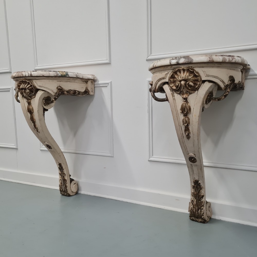 A pair of French nineteenth-century wall-mounted console tables with shaped marble tops and carved gilded single support legs.