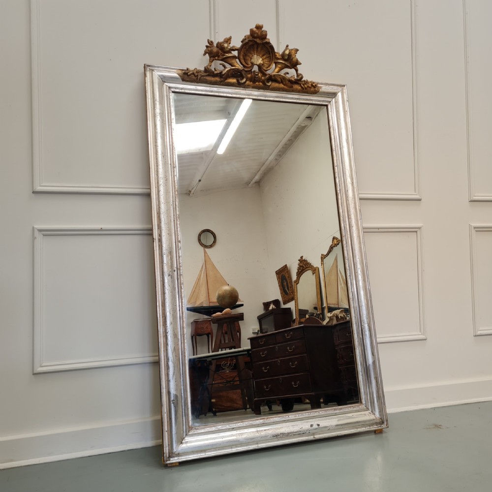 A large 19th-century rectangular French mirror featuring a silver gilded frame crowned with a carved gold Rococo shell cresting.