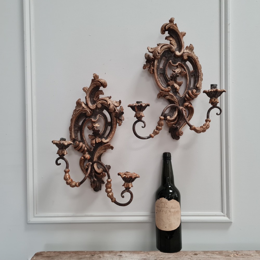 A pair of carved wood wall sconces featuring ornate scrollwork, aged silver leaf finish, and twin candle arms. View II