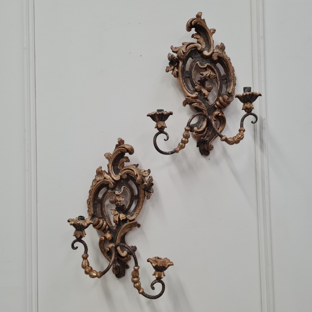 A pair of carved wood wall sconces featuring ornate scrollwork, aged silver leaf finish, and twin candle arms. View VI