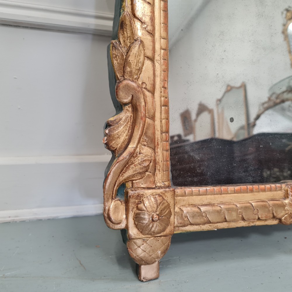 An 18th-century French gilded wooden mirror featuring a carved ornate crest with bow and garland motifs set against a blue background, enclosing a foxed rectangular mirror plate. View II
