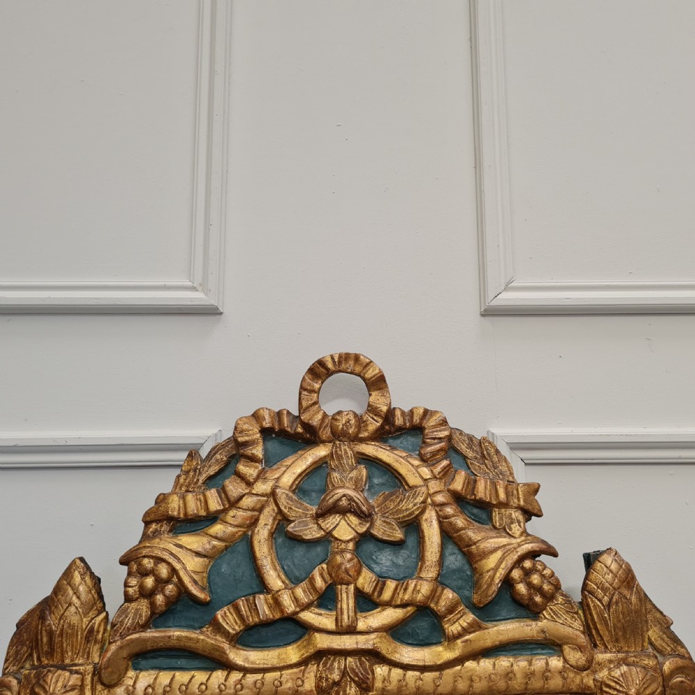 An 18th-century French gilded wooden mirror featuring a carved ornate crest with bow and garland motifs set against a blue background, enclosing a foxed rectangular mirror plate. View III