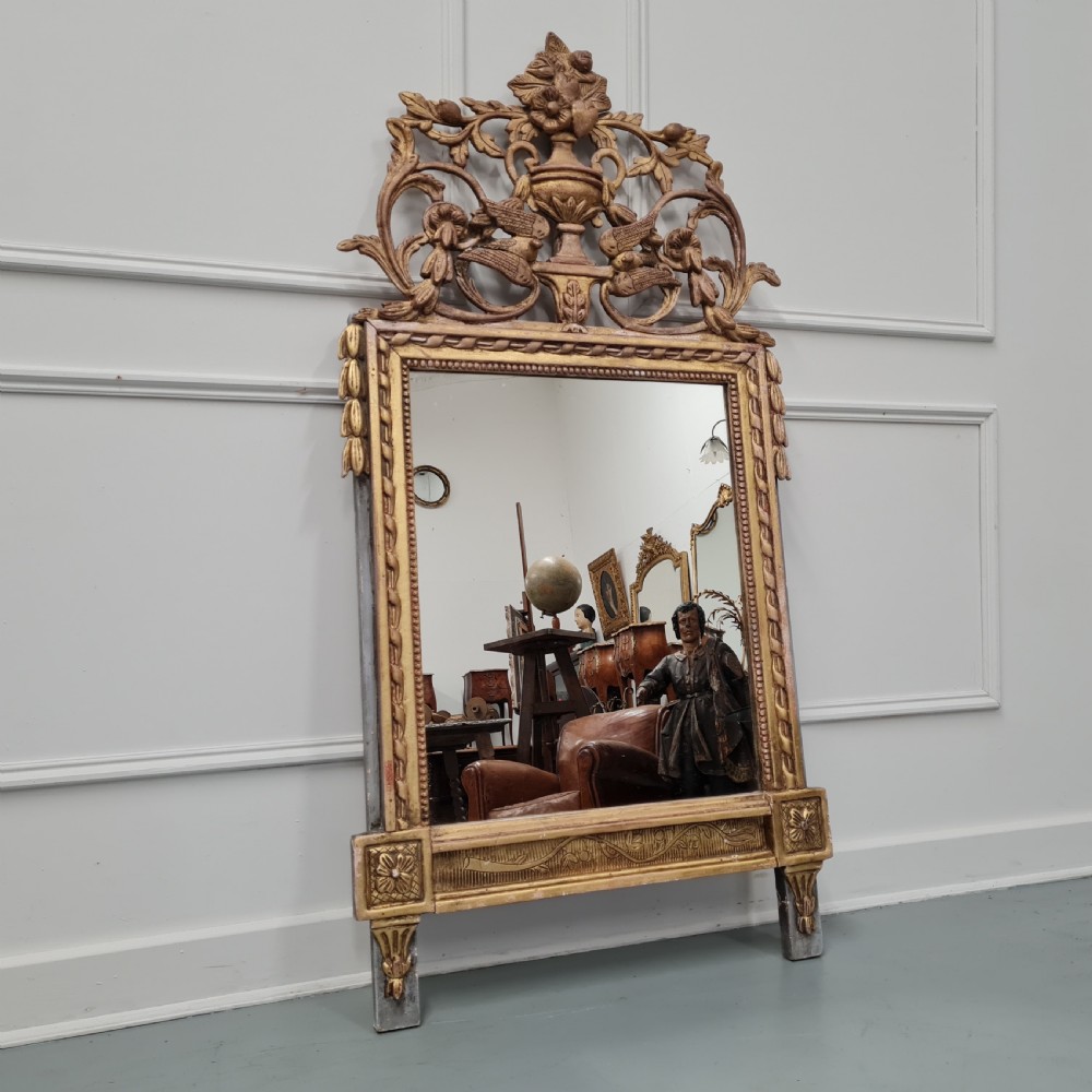A large antique French giltwood marriage mirror circa 1900 featuring an elaborate carved crest with an urn and bird motifs above a rectangular beaded frame.