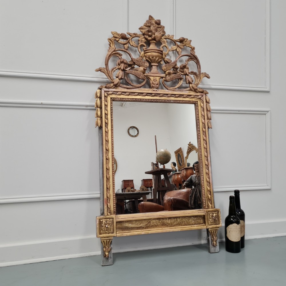A large antique French giltwood marriage mirror circa 1900 featuring an elaborate carved crest with an urn and bird motifs above a rectangular beaded frame. View V