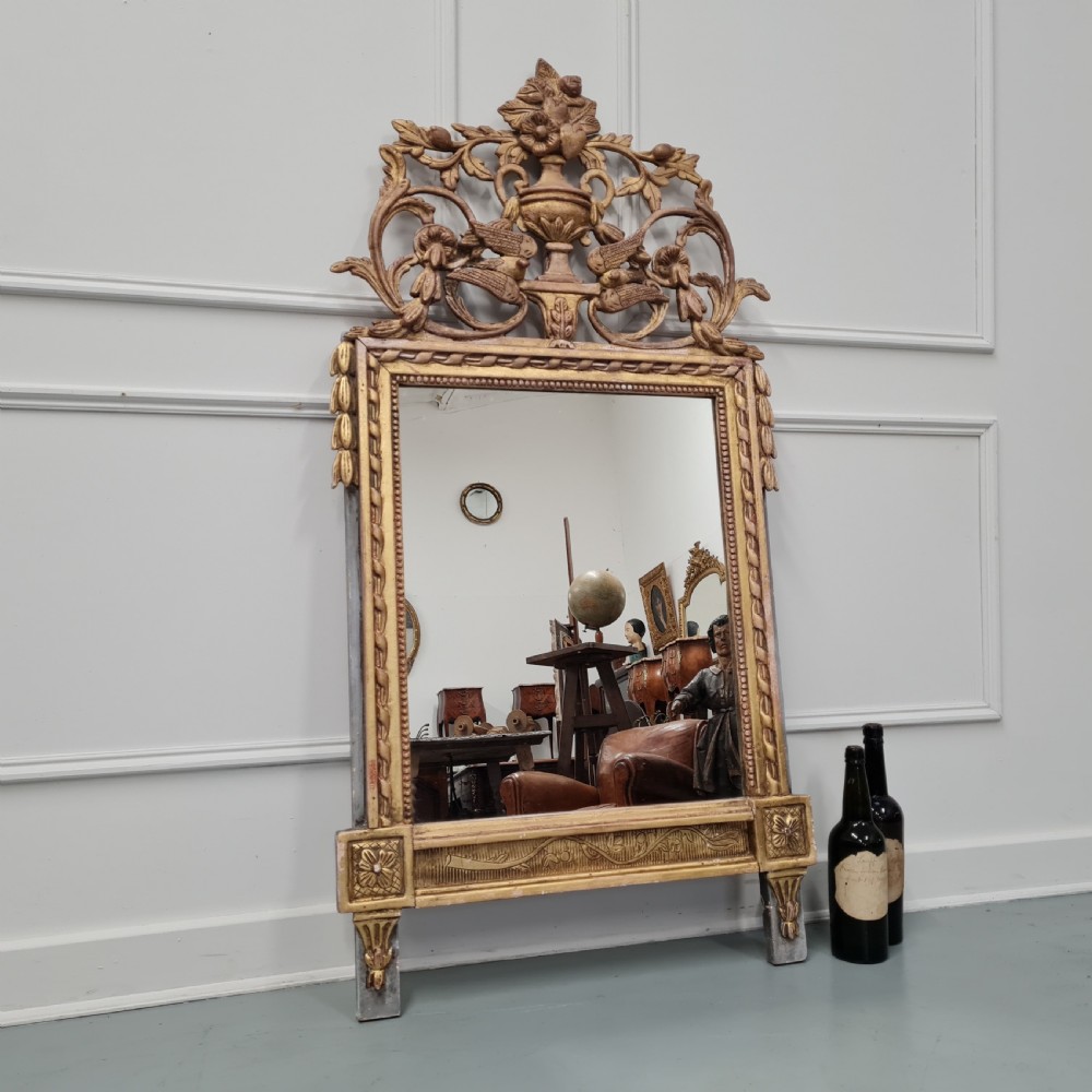 A large antique French giltwood marriage mirror circa 1900 featuring an elaborate carved crest with an urn and bird motifs above a rectangular beaded frame. View VI