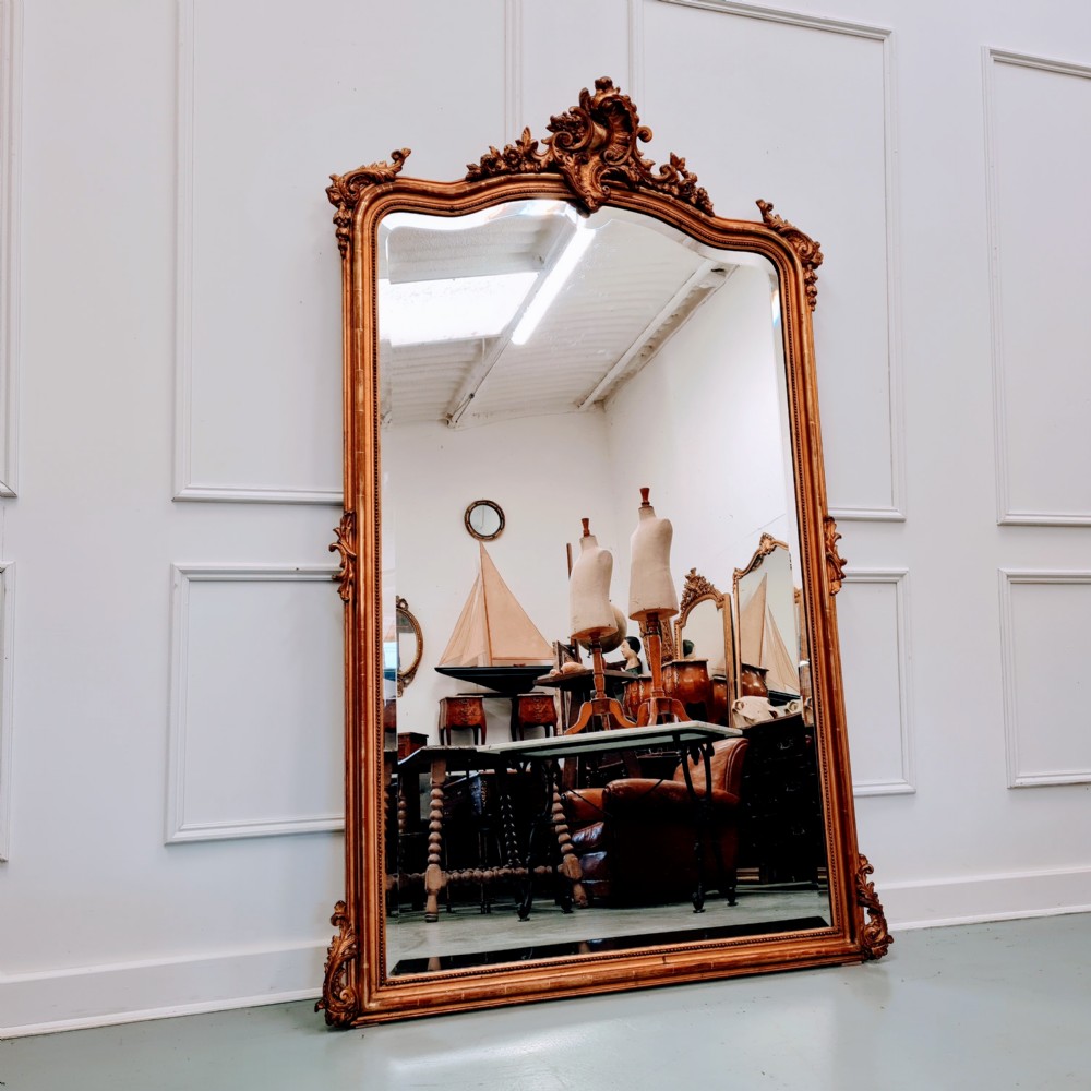 A large late nineteenth-century French wall mirror featuring a gilded frame with carved rococo cresting and scrollwork details.