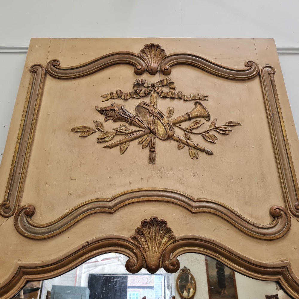 A tall French trumeau mirror featuring a cream painted frame with gilt carved moulding, an upper relief panel displaying a trophy motif, and rectangular glass below. View II