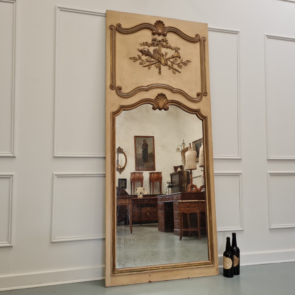 A tall French trumeau mirror featuring a cream painted frame with gilt carved moulding, an upper relief panel displaying a trophy motif, and rectangular glass below. View III