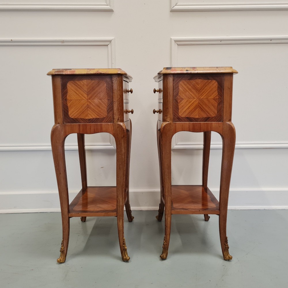 A pair of French 1930s serpentine bedside tables featuring marble tops, chevron veneer drawers, cabriole legs with brass mounts, and a lower shelf. View V
