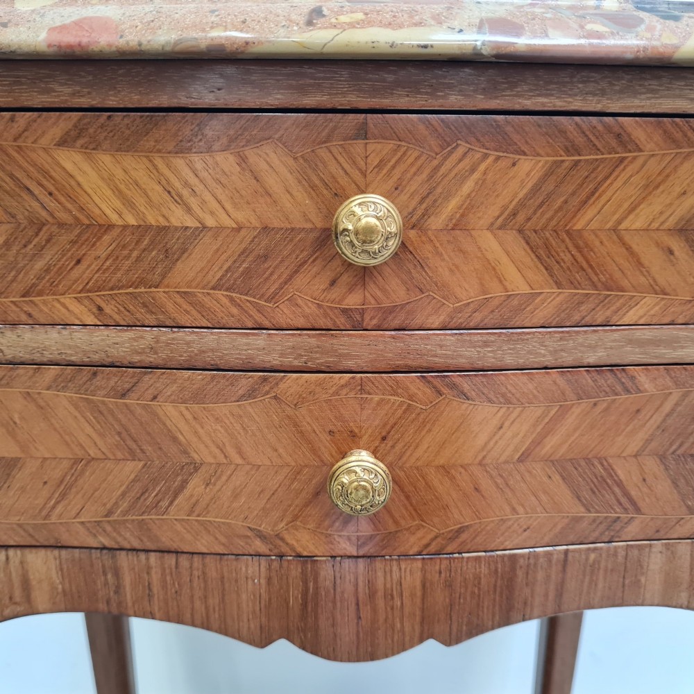 A pair of French 1930s serpentine bedside tables featuring marble tops, chevron veneer drawers, cabriole legs with brass mounts, and a lower shelf. View X