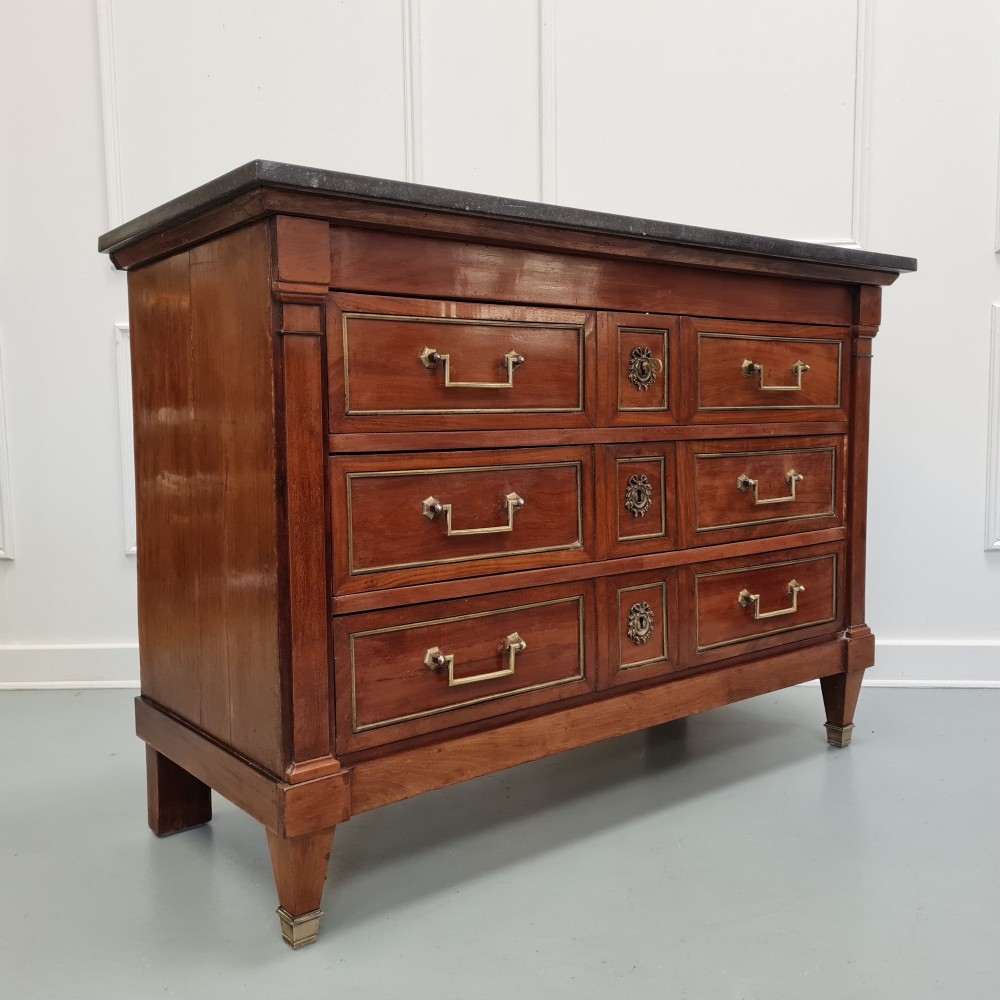 A French Empire mahogany commode featuring three wide drawers with brass handles, central keyhole escutcheons, and a dark marble top. View II