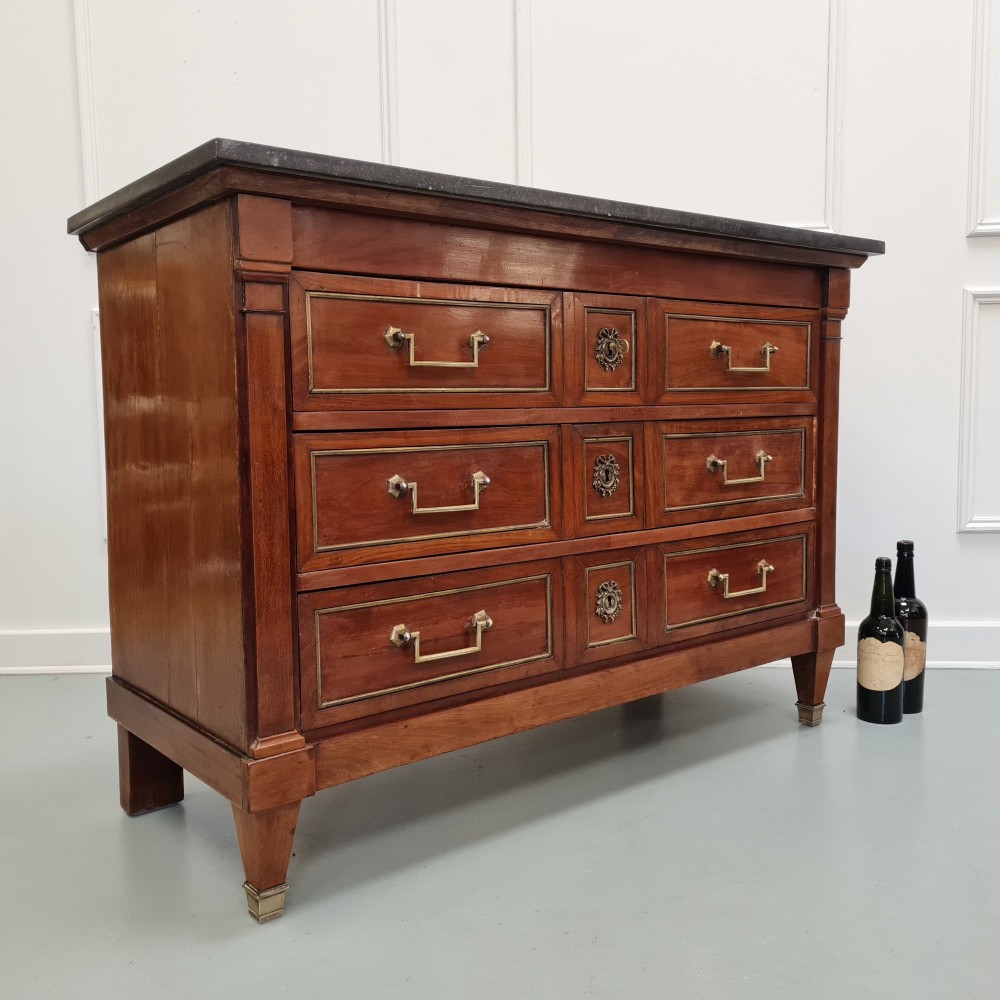 A French Empire mahogany commode featuring three wide drawers with brass handles, central keyhole escutcheons, and a dark marble top. View III