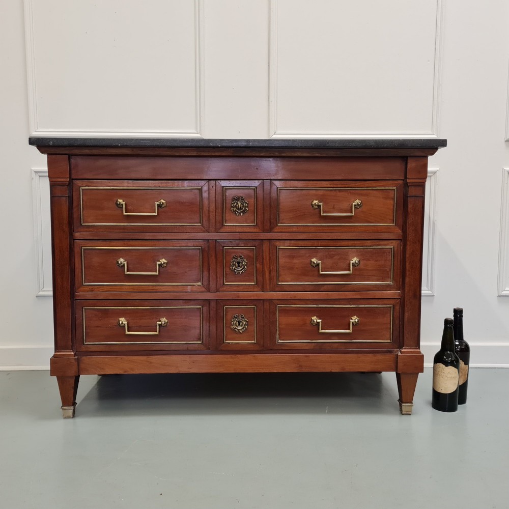 A French Empire mahogany commode featuring three wide drawers with brass handles, central keyhole escutcheons, and a dark marble top. View IV
