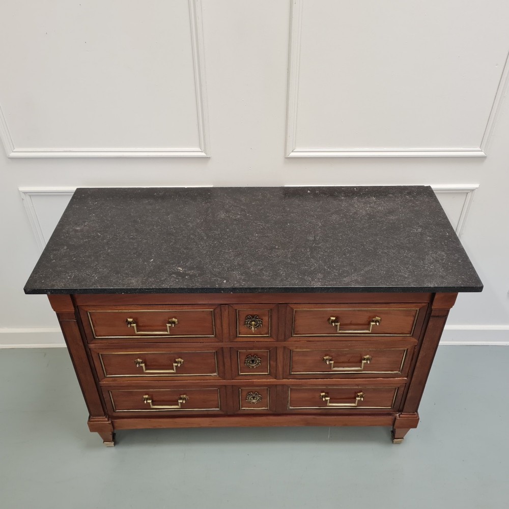 A French Empire mahogany commode featuring three wide drawers with brass handles, central keyhole escutcheons, and a dark marble top. View V
