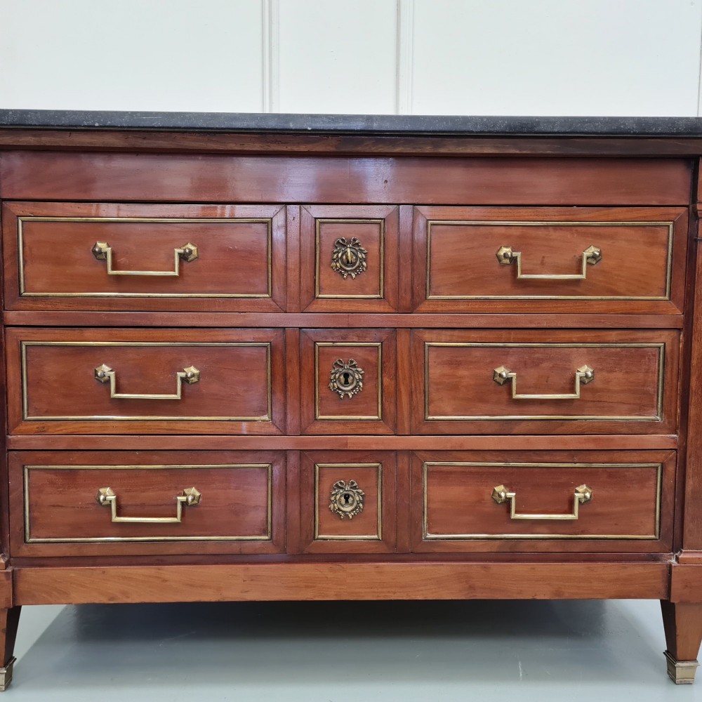 A French Empire mahogany commode featuring three wide drawers with brass handles, central keyhole escutcheons, and a dark marble top. View VII