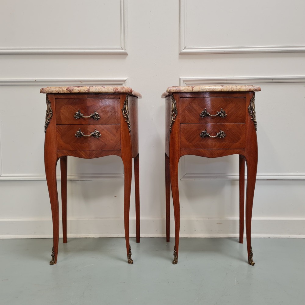 A pair of French 1930s bedside tables featuring variegated marble tops, walnut parquetry drawers, gilt brass mounts, and slender cabriole legs.