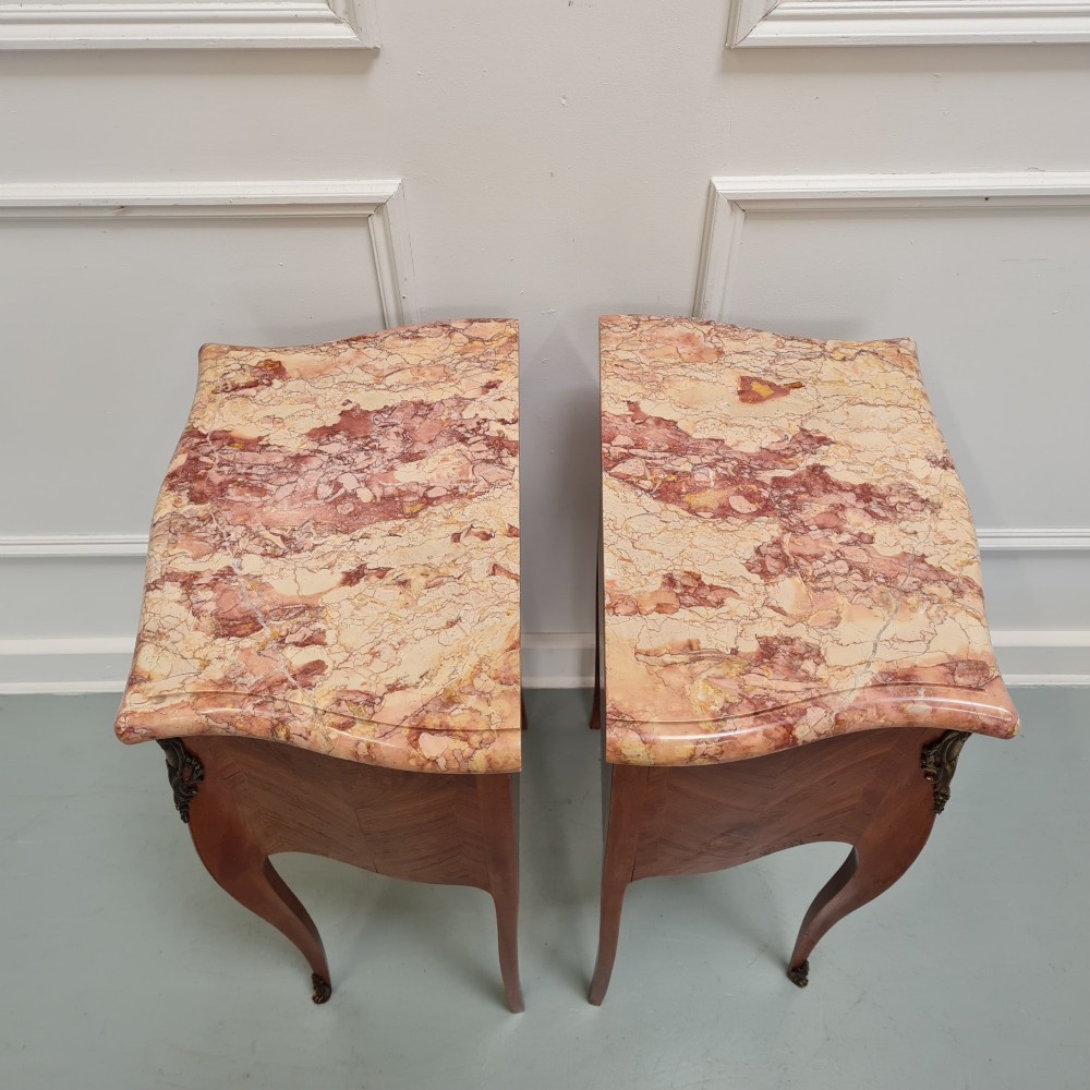 A pair of French 1930s bedside tables featuring variegated marble tops, walnut parquetry drawers, gilt brass mounts, and slender cabriole legs. View V