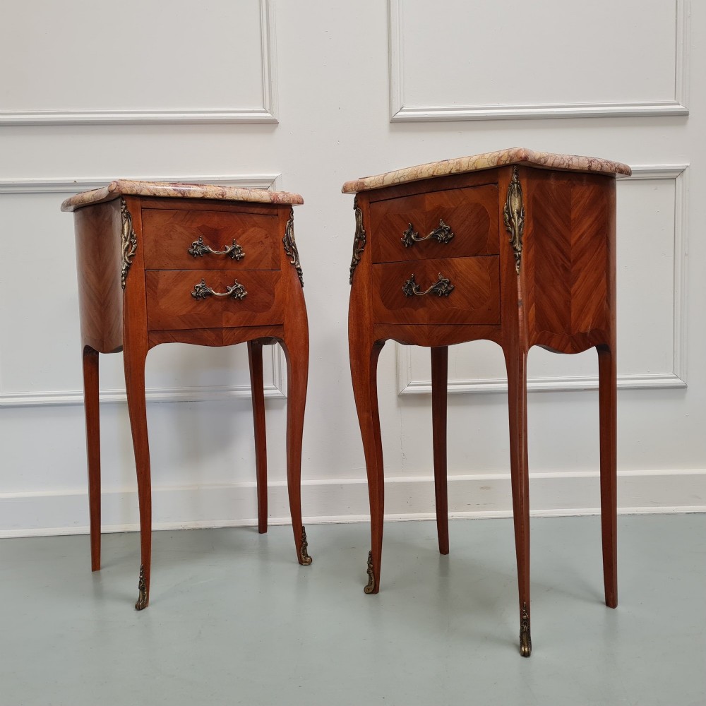 A pair of French 1930s bedside tables featuring variegated marble tops, walnut parquetry drawers, gilt brass mounts, and slender cabriole legs. View VI