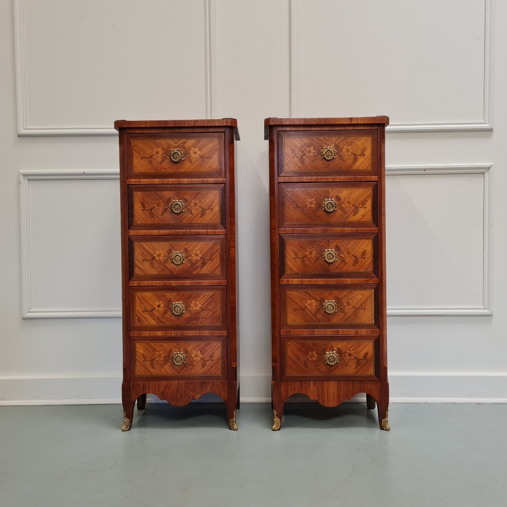 A pair of tall French-style wooden bedside cabinets with floral marquetry inlay, five drawers each, brass rosette handles, and curved cabriole legs with brass feet.