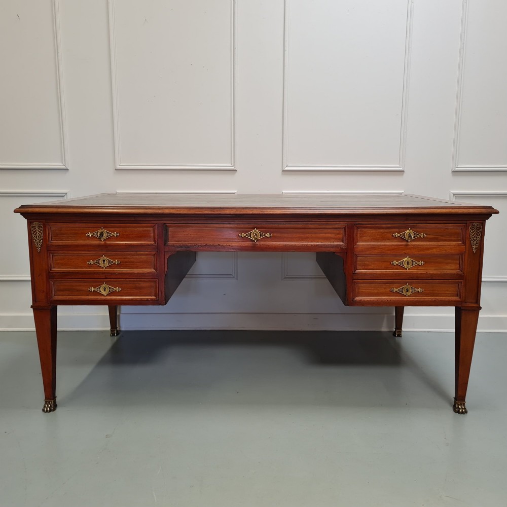 A large Empire style mahogany writing desk featuring a leather inset top, brass mounts, ornate escutcheons, and tapered square legs with brass feet.