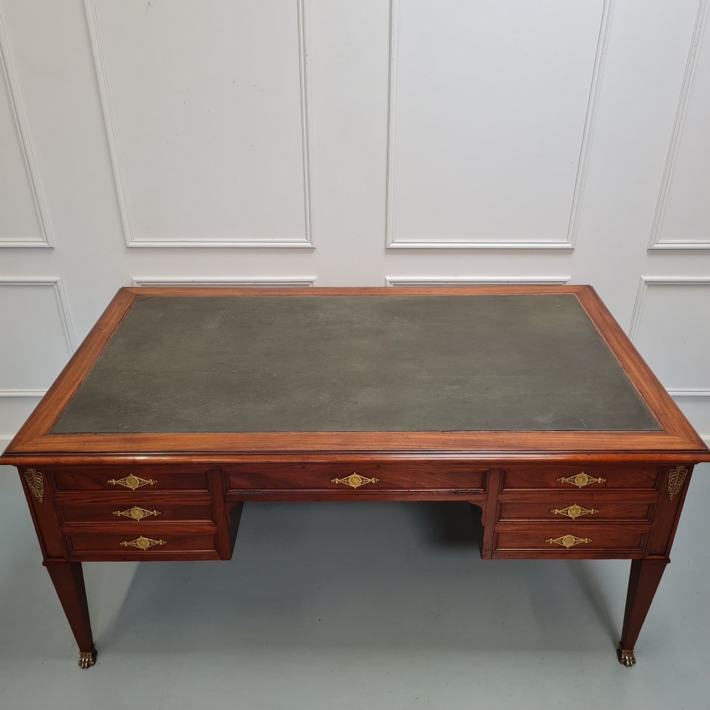 A large Empire style mahogany writing desk featuring a leather inset top, brass mounts, ornate escutcheons, and tapered square legs with brass feet. View IV