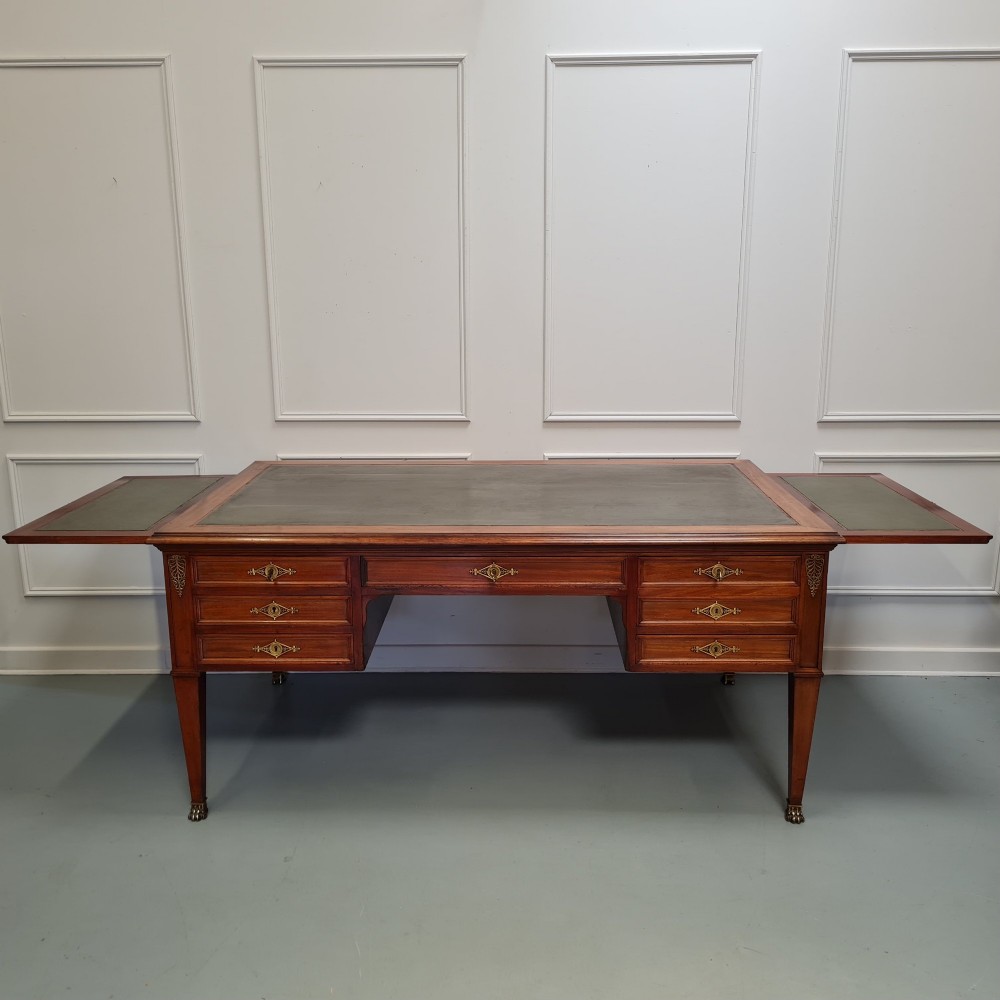 A large Empire style mahogany writing desk featuring a leather inset top, brass mounts, ornate escutcheons, and tapered square legs with brass feet. View V