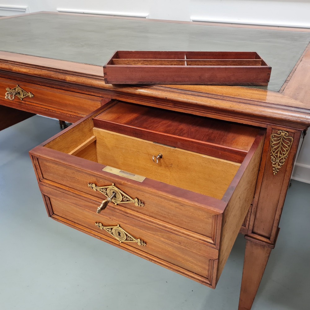 A large Empire style mahogany writing desk featuring a leather inset top, brass mounts, ornate escutcheons, and tapered square legs with brass feet. View VI