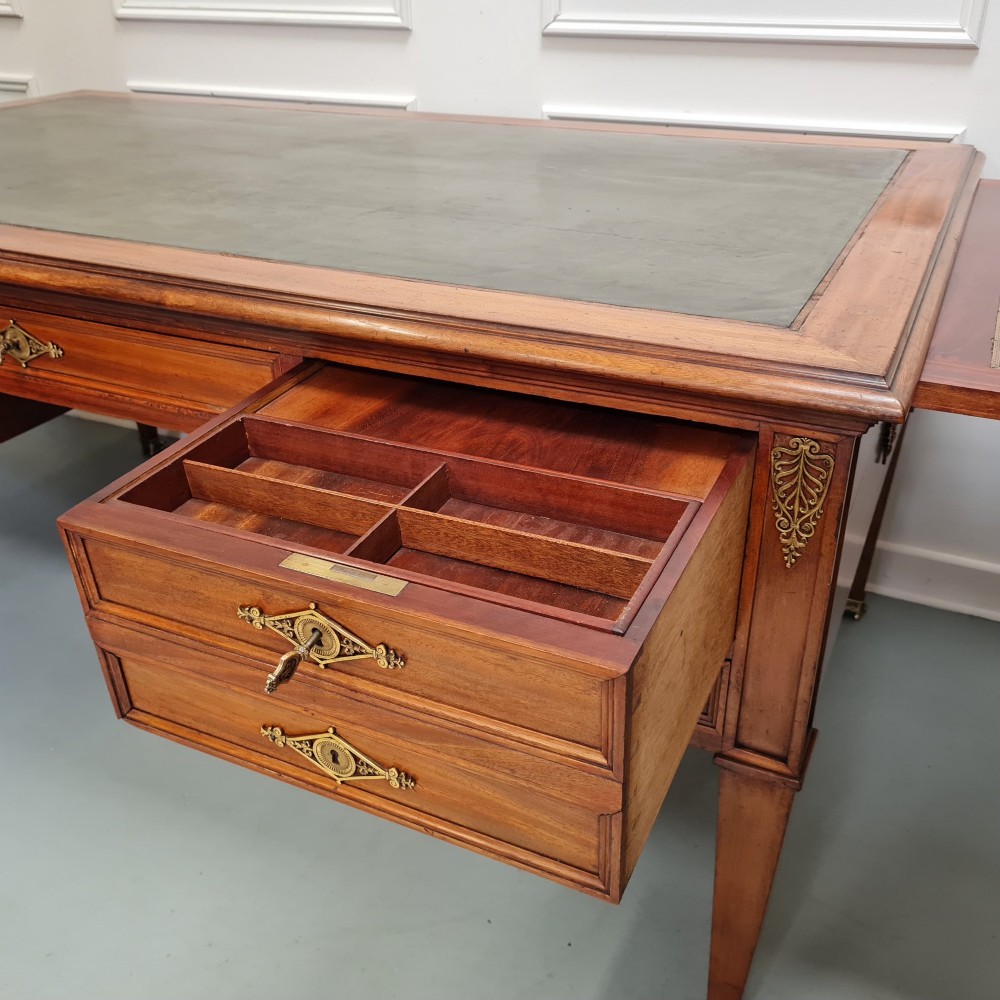 A large Empire style mahogany writing desk featuring a leather inset top, brass mounts, ornate escutcheons, and tapered square legs with brass feet. View VII