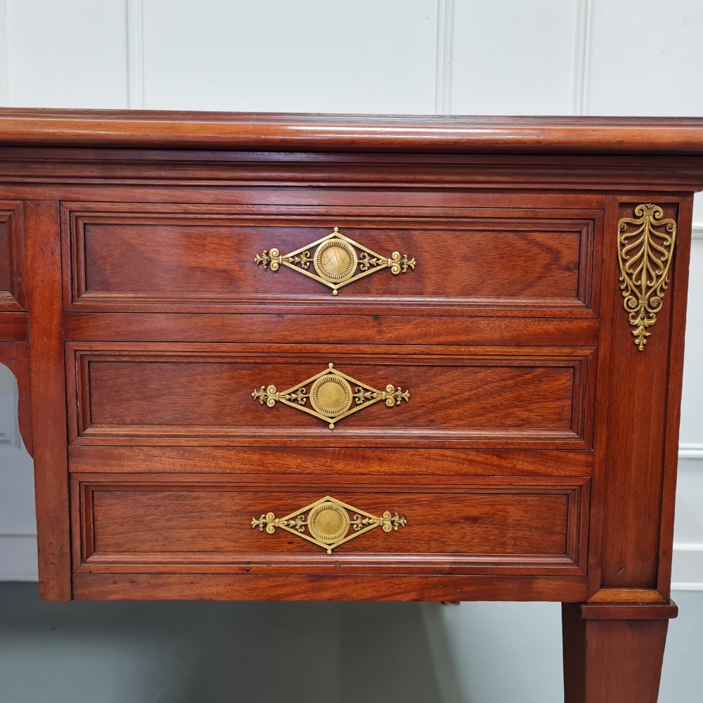 A large Empire style mahogany writing desk featuring a leather inset top, brass mounts, ornate escutcheons, and tapered square legs with brass feet. View IX