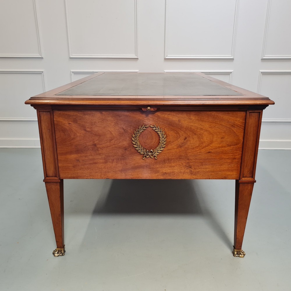 A large Empire style mahogany writing desk featuring a leather inset top, brass mounts, ornate escutcheons, and tapered square legs with brass feet. View X