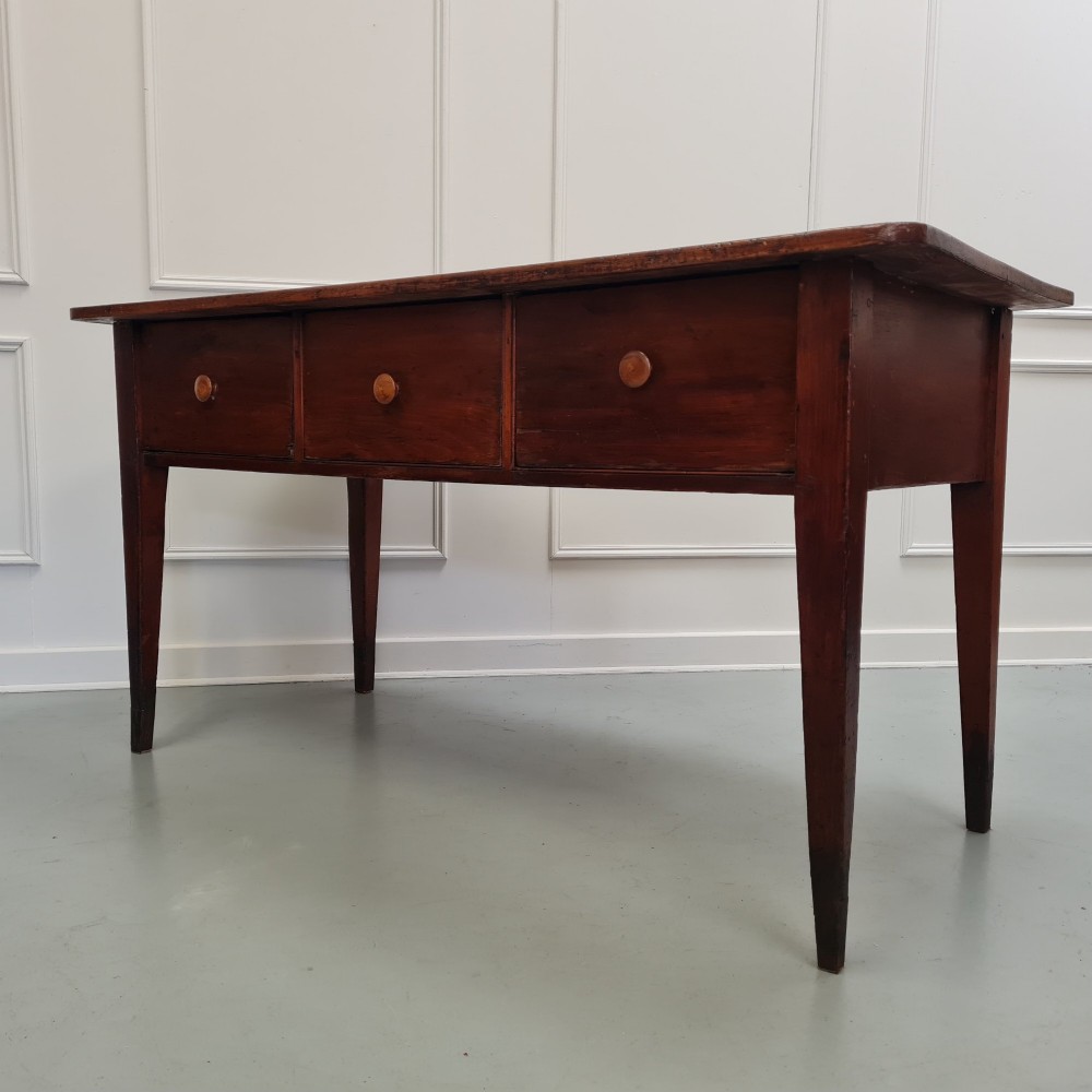 A mid-nineteenth-century warm brown wooden serving table featuring three drawers with turned knobs and four tapered square legs. View II