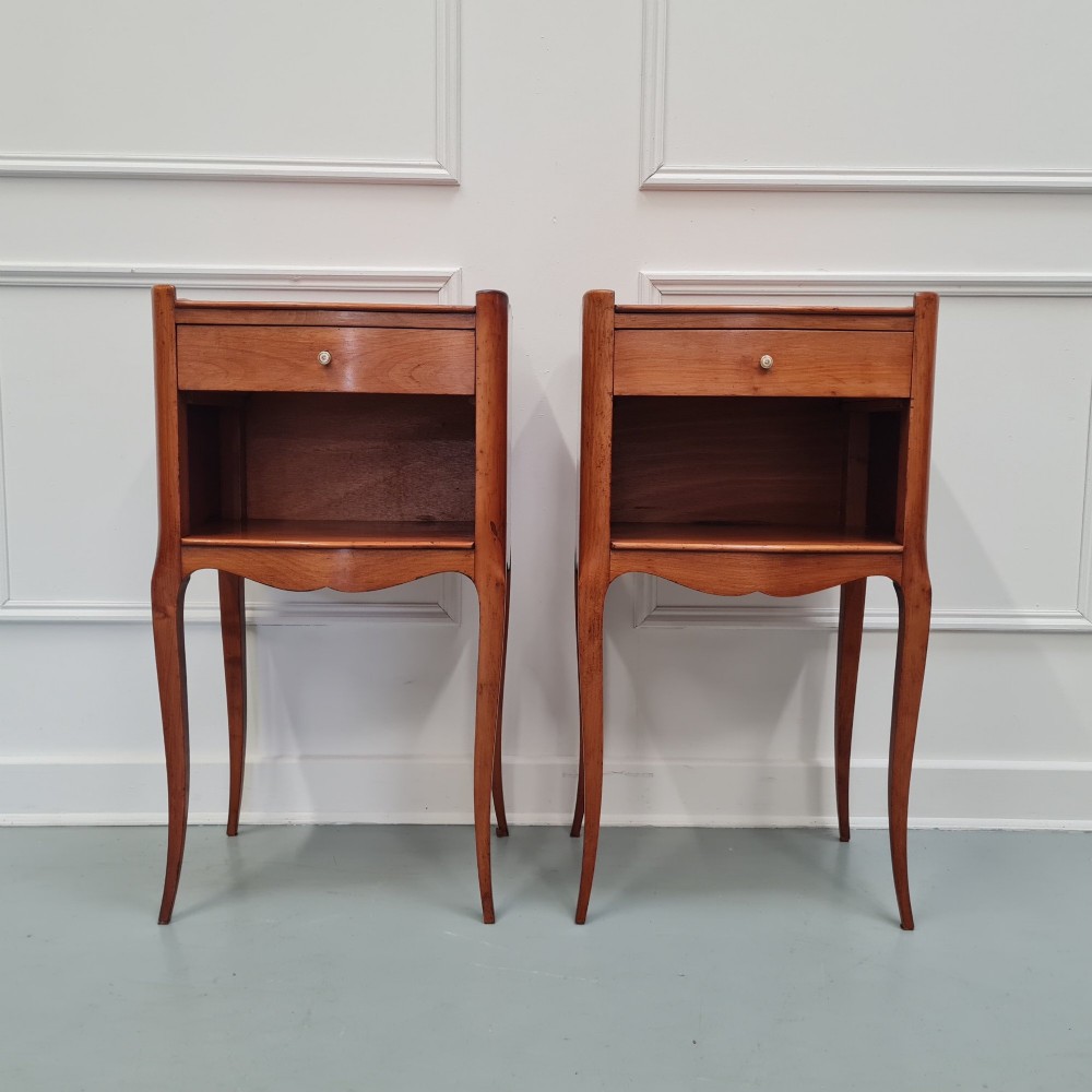 A pair of French cherry wood bedside tables featuring single drawers with small pull knobs, open lower shelves, and slender cabriole legs.